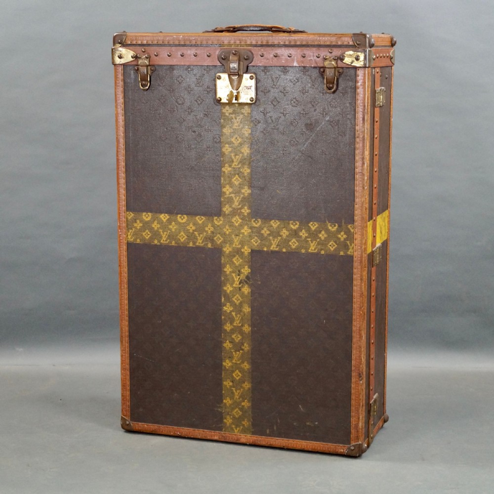 An upright dark brown monogram canvas trunk featuring a yellow painted cross band, leather edging, and brass latches. View IX