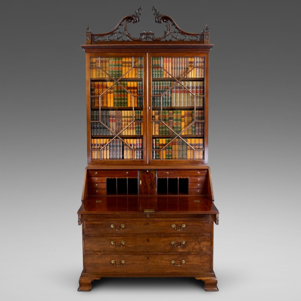 A George III mahogany bureau bookcase featuring a carved fretwork pediment, two astragal glazed upper doors, a sloping fall-front desk, and four graduated drawers with brass handles. View II