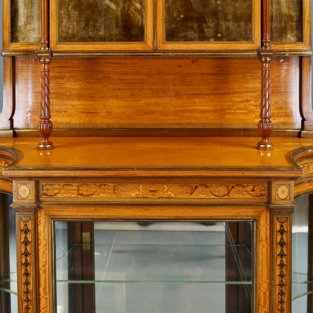 An antique satinwood display cabinet featuring marquetry inlays, glazed double-tier doors, turned support columns, and an ornamental top finial. View III