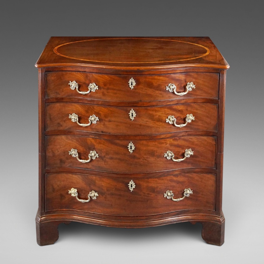 A George III flame mahogany serpentine chest of drawers featuring four graduated drawers with brass handles, keyhole escutcheons, bracket feet, and an oval inlaid top.