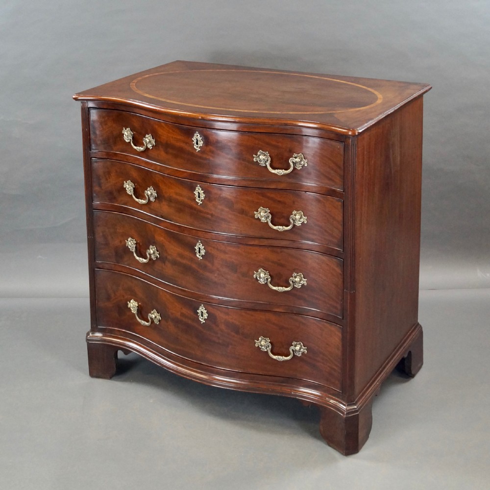 A George III flame mahogany serpentine chest of drawers featuring four graduated drawers with brass handles, keyhole escutcheons, bracket feet, and an oval inlaid top. View II
