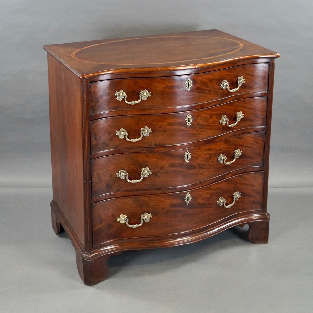 A George III flame mahogany serpentine chest of drawers featuring four graduated drawers with brass handles, keyhole escutcheons, bracket feet, and an oval inlaid top. View III