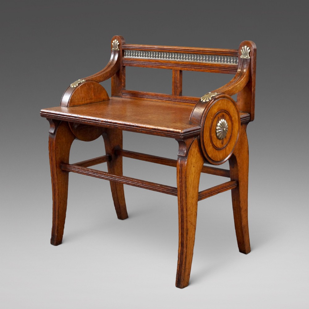 An oak hall seat featuring curved armrests with brass shell mounts, circular side roundels with central brass bosses, and a gallery-backed top rail.