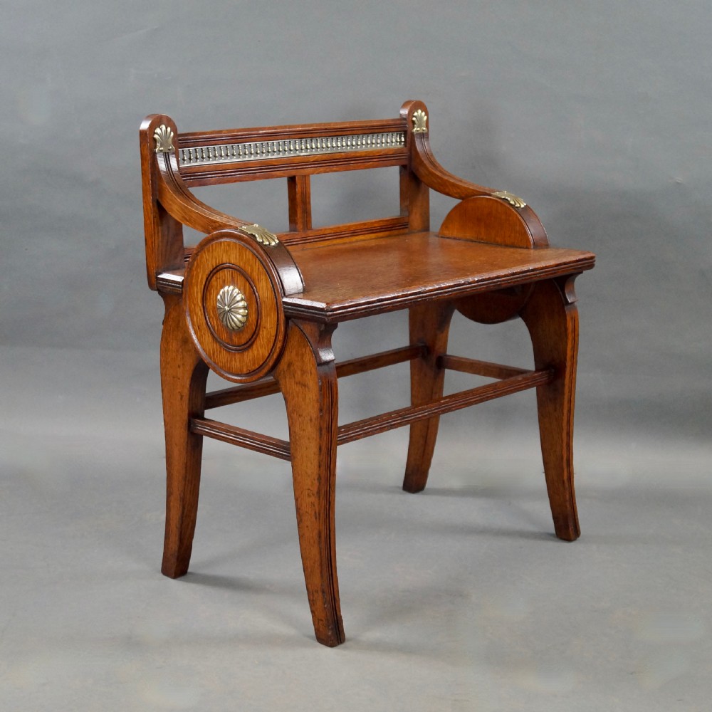 An oak hall seat featuring curved armrests with brass shell mounts, circular side roundels with central brass bosses, and a gallery-backed top rail. View II