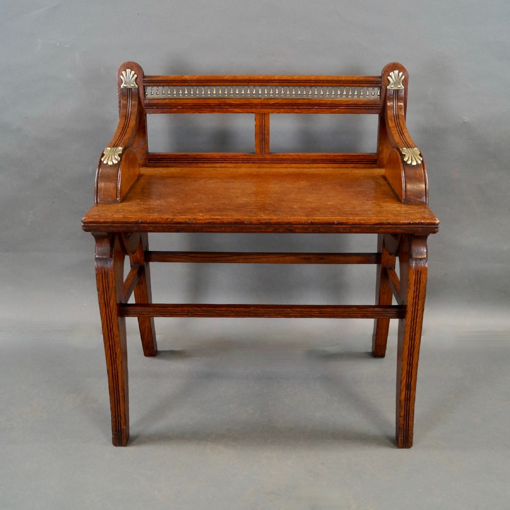 An oak hall seat featuring curved armrests with brass shell mounts, circular side roundels with central brass bosses, and a gallery-backed top rail. View V