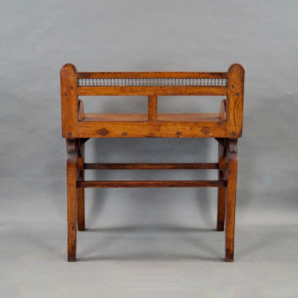 An oak hall seat featuring curved armrests with brass shell mounts, circular side roundels with central brass bosses, and a gallery-backed top rail. View VI