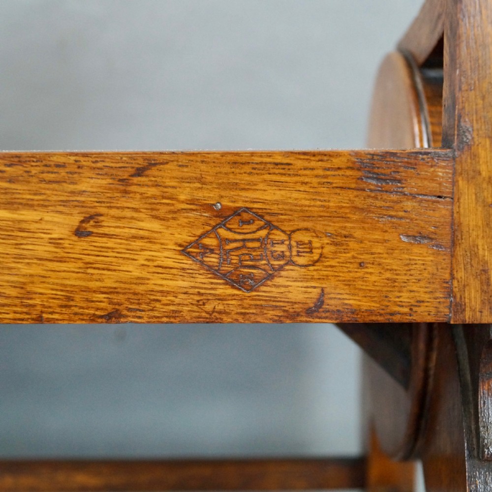 An oak hall seat featuring curved armrests with brass shell mounts, circular side roundels with central brass bosses, and a gallery-backed top rail. View VII
