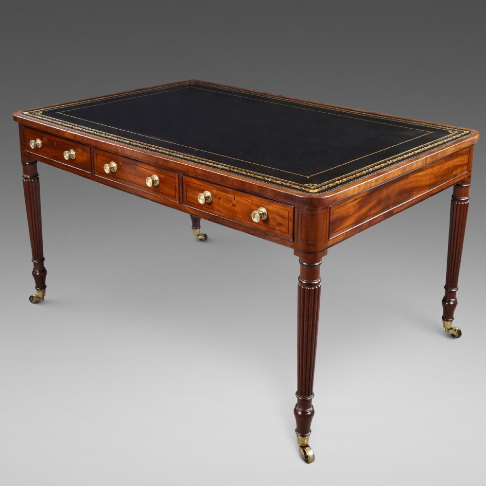 A George III mahogany partners writing table featuring a gold-tooled leather top, three drawers with brass knob handles, and fluted legs on brass castors. View II