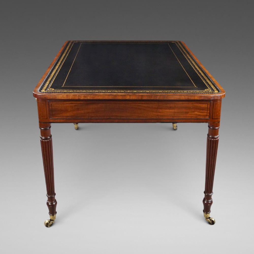 A George III mahogany partners writing table featuring a gold-tooled leather top, three drawers with brass knob handles, and fluted legs on brass castors. View III
