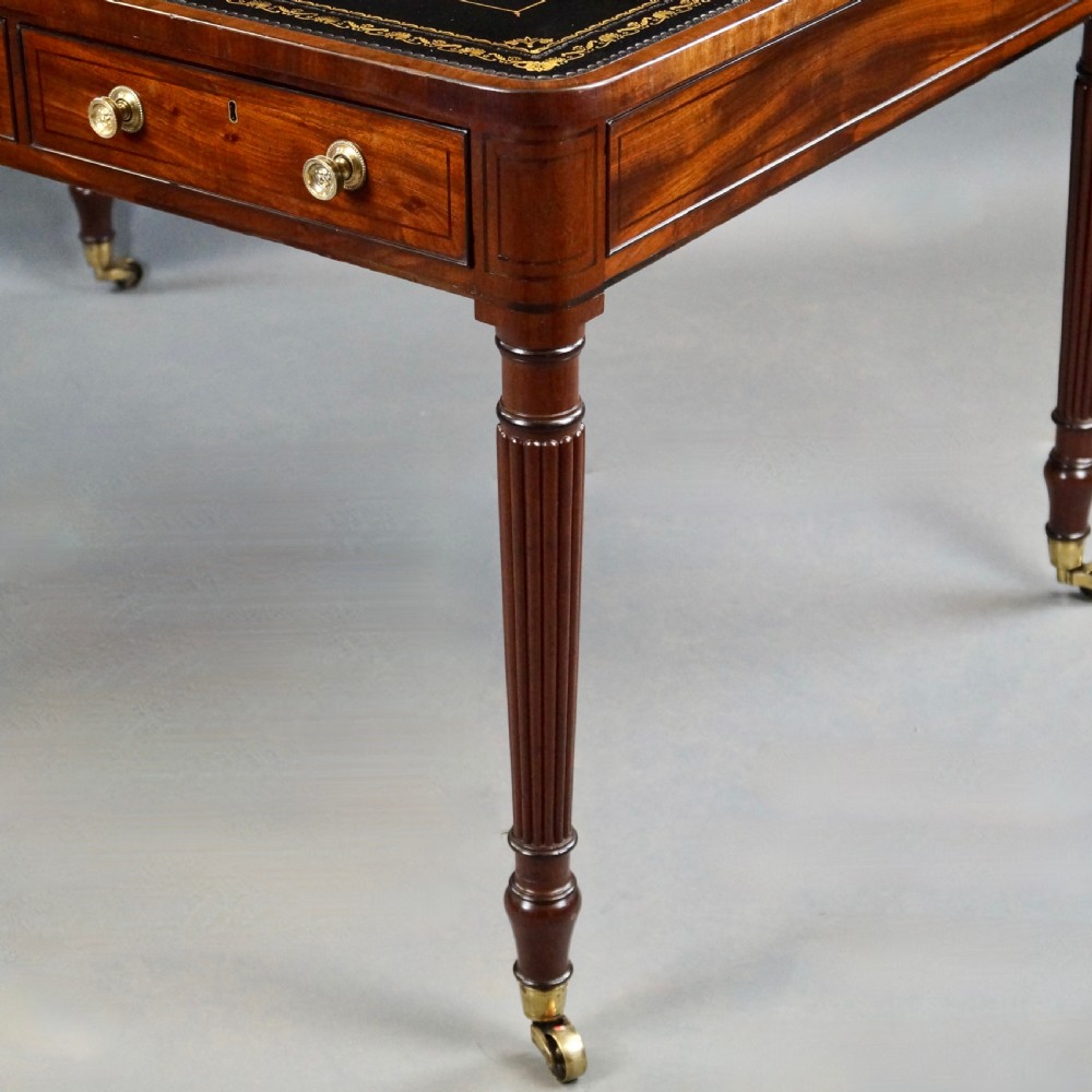 A George III mahogany partners writing table featuring a gold-tooled leather top, three drawers with brass knob handles, and fluted legs on brass castors. View V