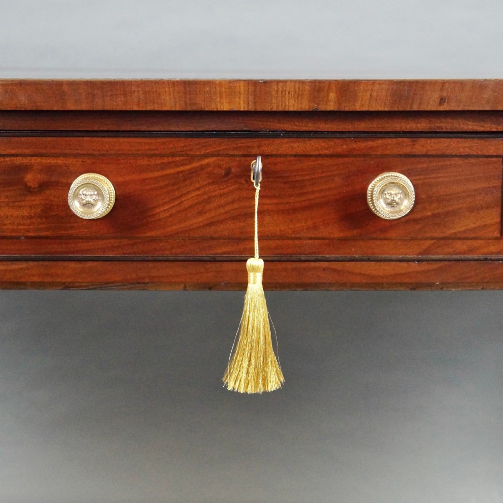 A George III mahogany partners writing table featuring a gold-tooled leather top, three drawers with brass knob handles, and fluted legs on brass castors. View VII