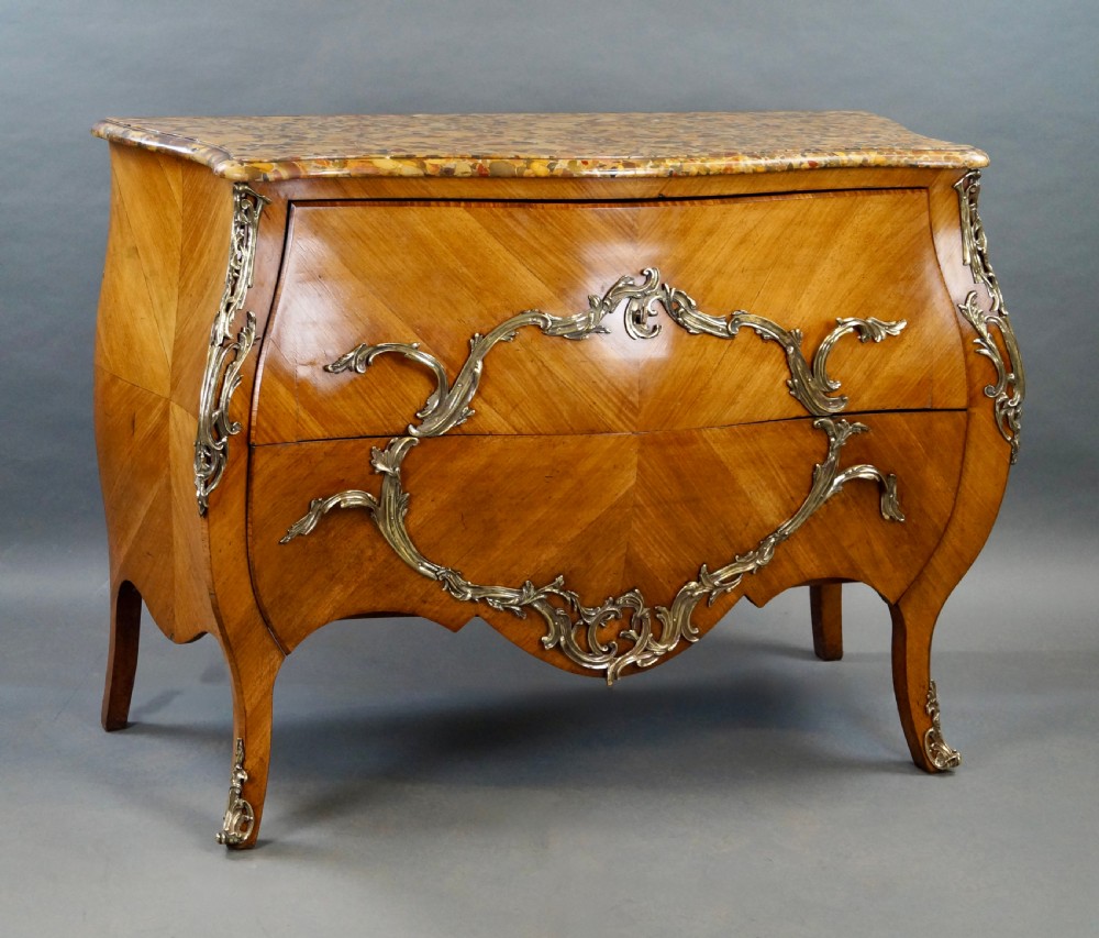 A nineteenth-century French bombe commode featuring chevron parquetry veneer, ornate scrollwork metal mounts, and a shaped marble top. View V
