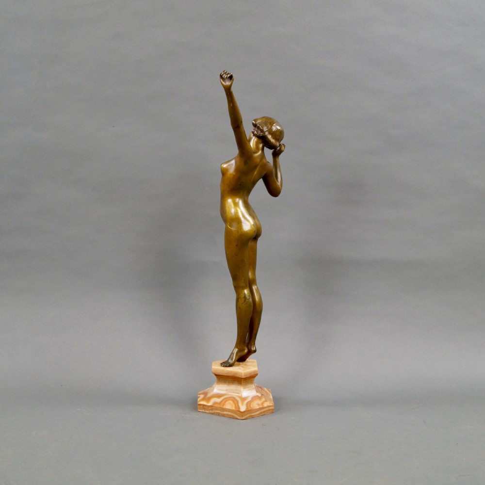 A stylised Art Deco gilt bronze statuette depicting a standing female nude with raised arms, mounted on a stepped onyx plinth base. View II