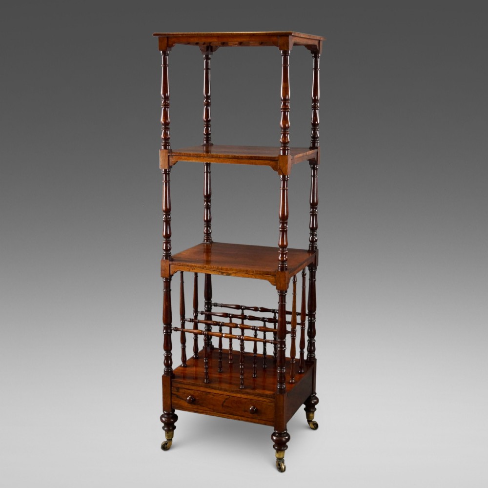 A tall four-tier antique rosewood whatnot featuring slender turned upright supports, a spindle divider shelf, a lower drawer, and brass castors.