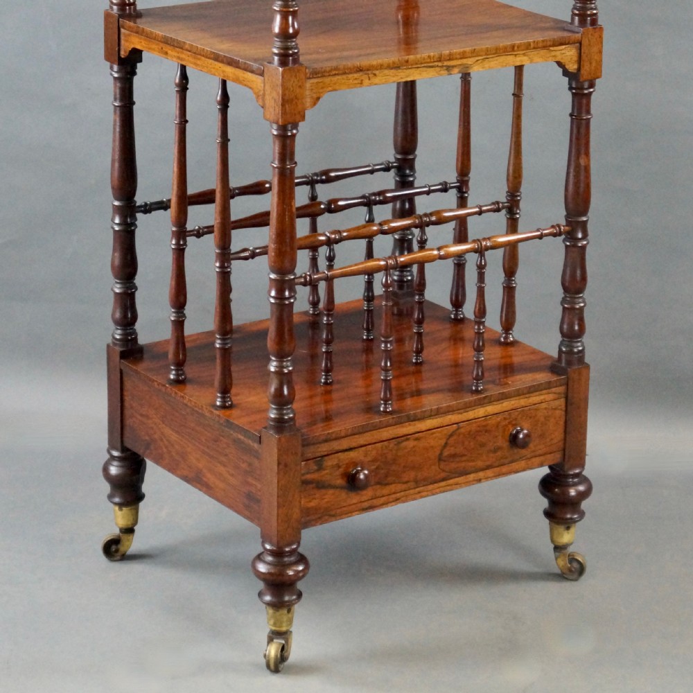A tall four-tier antique rosewood whatnot featuring slender turned upright supports, a spindle divider shelf, a lower drawer, and brass castors. View II