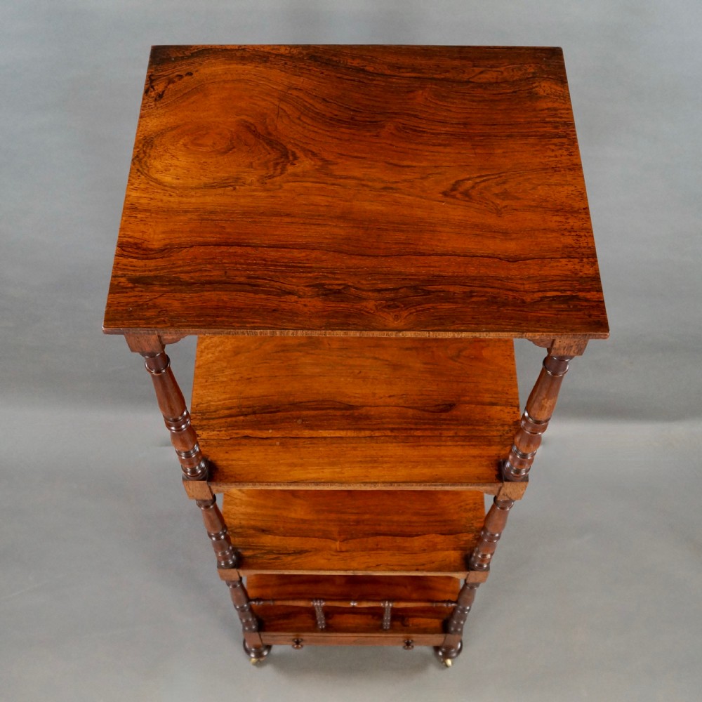 A tall four-tier antique rosewood whatnot featuring slender turned upright supports, a spindle divider shelf, a lower drawer, and brass castors. View V