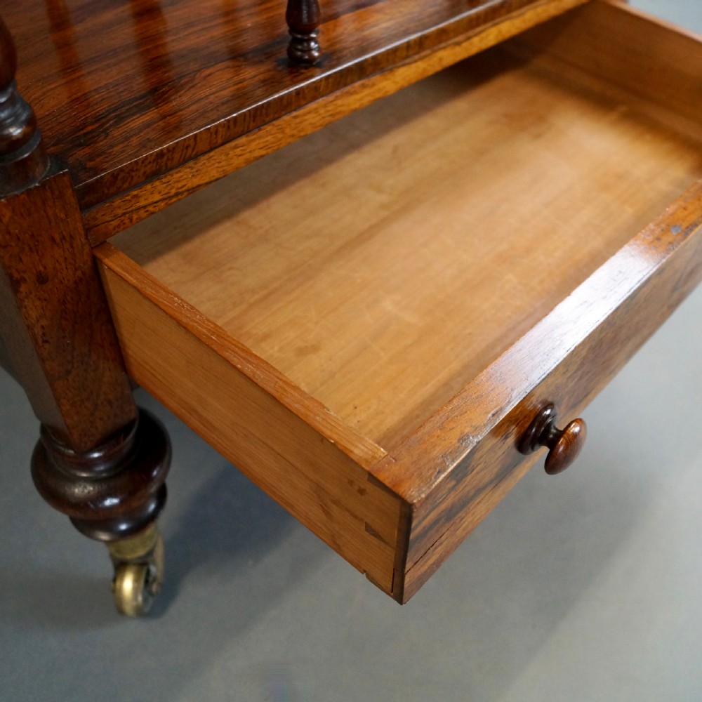 A tall four-tier antique rosewood whatnot featuring slender turned upright supports, a spindle divider shelf, a lower drawer, and brass castors. View VI
