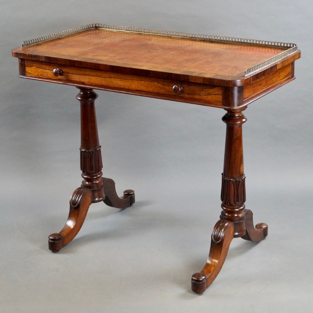 A Victorian rosewood writing table featuring a brass gallery rail around three edges, a front drawer with turned wooden knobs, and twin carved pedestal legs. View II