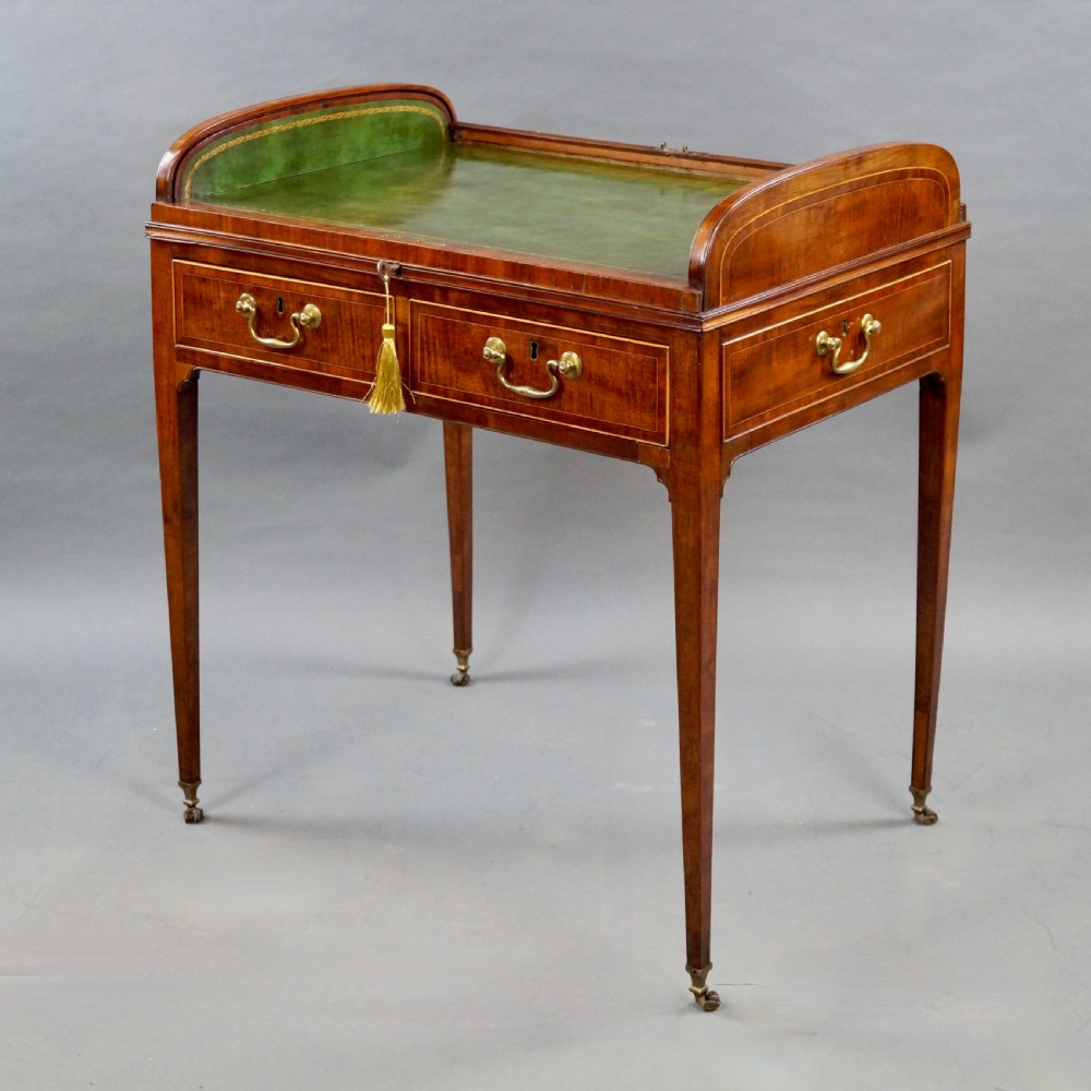 A George III mahogany tambour desk with a curved slatted roll top, drawer brass handles, fine inlay stringing, and square tapered legs fitted with brass castors. View II