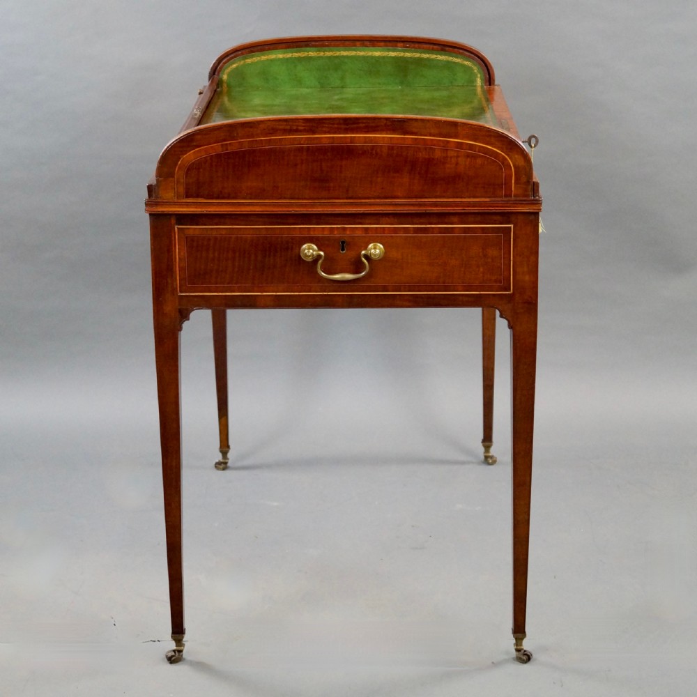 A George III mahogany tambour desk with a curved slatted roll top, drawer brass handles, fine inlay stringing, and square tapered legs fitted with brass castors. View III