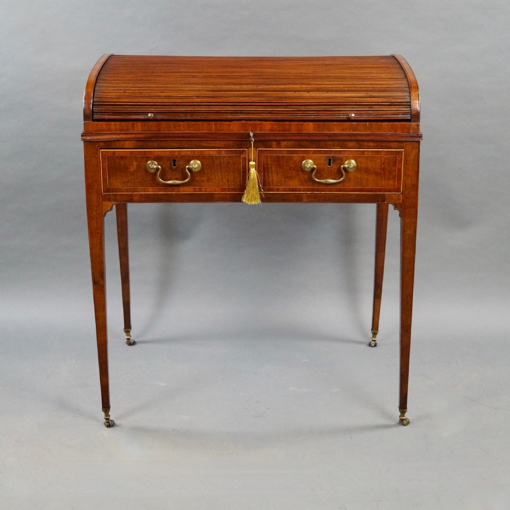 A George III mahogany tambour desk with a curved slatted roll top, drawer brass handles, fine inlay stringing, and square tapered legs fitted with brass castors. View V