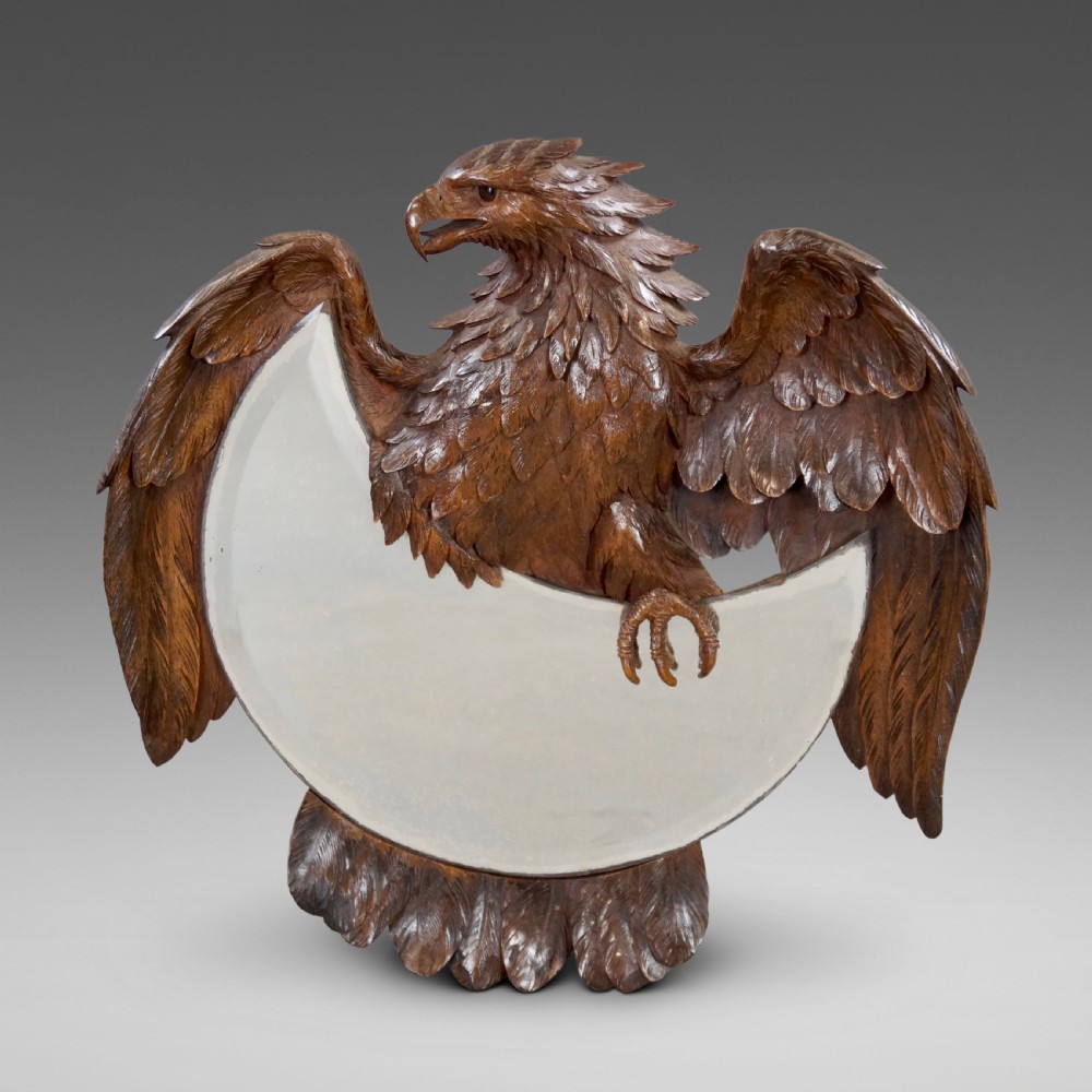 A carved wood wall mirror in the Black Forest style, featuring an eagle with outstretched wings surrounding a crescent moon-shaped mirror plate.