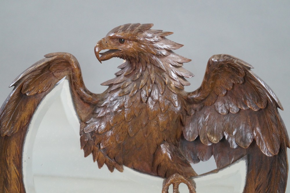 A carved wood wall mirror in the Black Forest style, featuring an eagle with outstretched wings surrounding a crescent moon-shaped mirror plate. View II