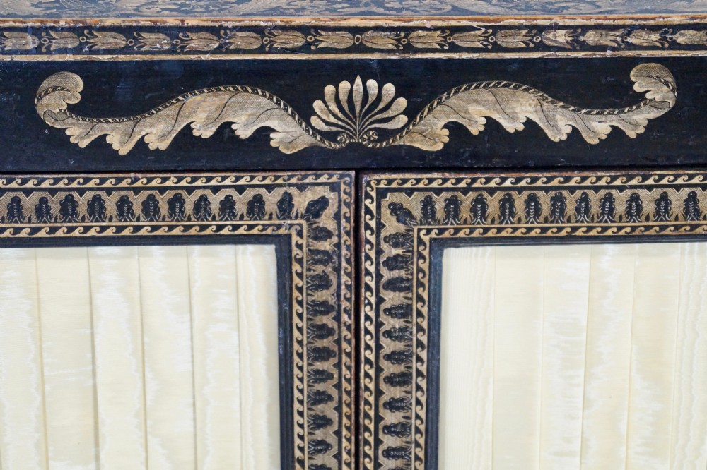 A Regency period black pen-work side cabinet featuring gold vine motifs, pleated yellow silk door panels, and gilded paw feet. View II