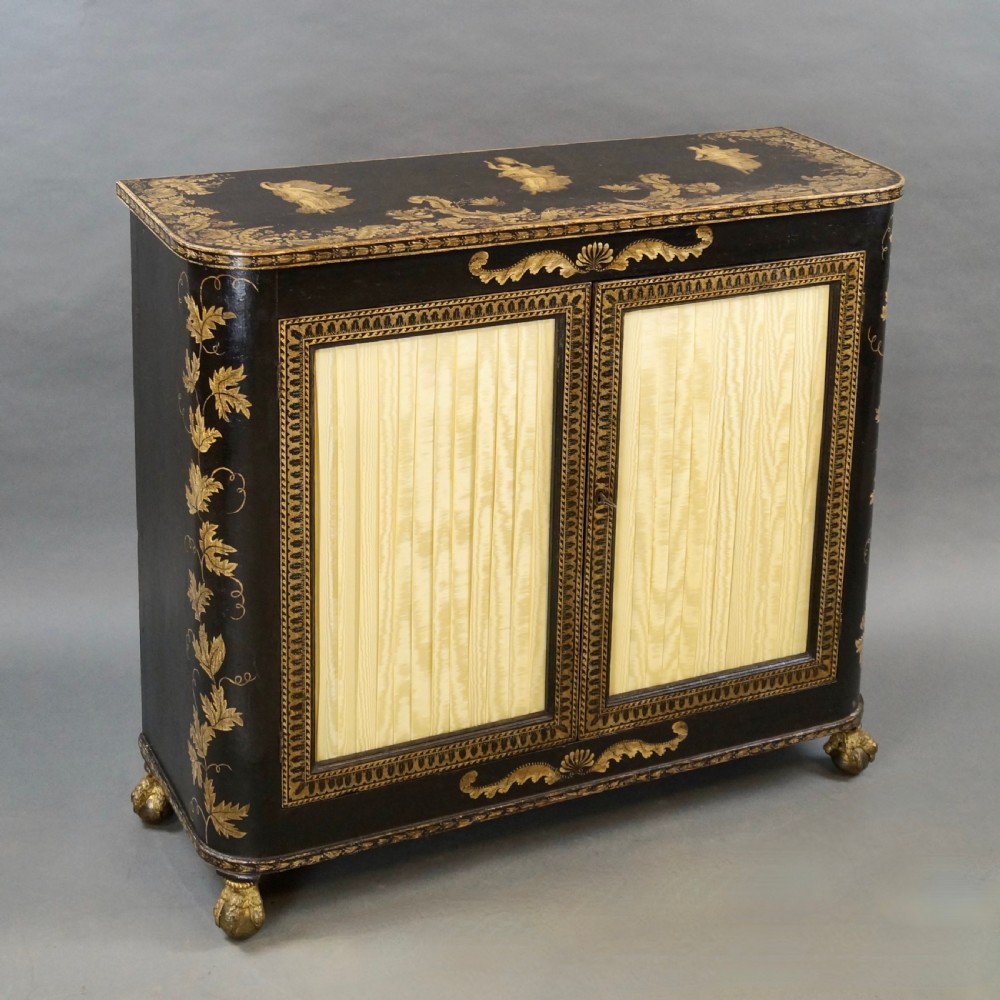 A Regency period black pen-work side cabinet featuring gold vine motifs, pleated yellow silk door panels, and gilded paw feet. View VI