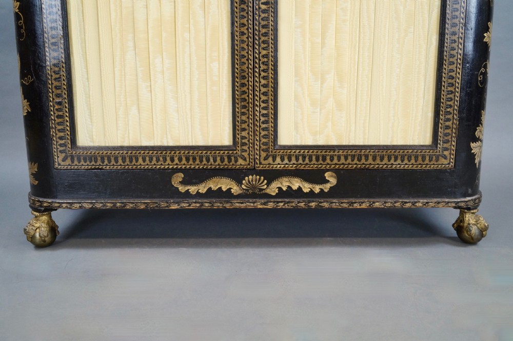 A Regency period black pen-work side cabinet featuring gold vine motifs, pleated yellow silk door panels, and gilded paw feet. View VII
