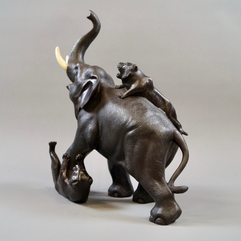 A dark brown patinated bronze okimono sculpture depicting an elephant fighting two tigers, featuring inlaid light tusks. View II