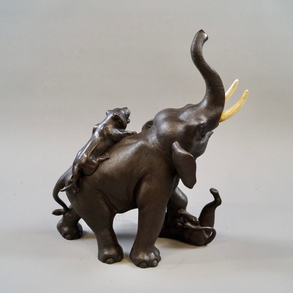 A dark brown patinated bronze okimono sculpture depicting an elephant fighting two tigers, featuring inlaid light tusks. View III