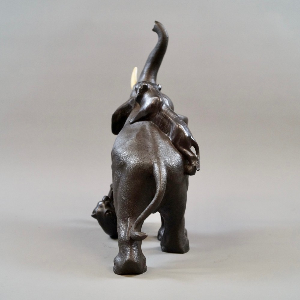 A dark brown patinated bronze okimono sculpture depicting an elephant fighting two tigers, featuring inlaid light tusks. View V