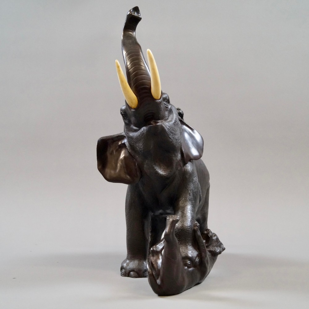 A dark brown patinated bronze okimono sculpture depicting an elephant fighting two tigers, featuring inlaid light tusks. View VI