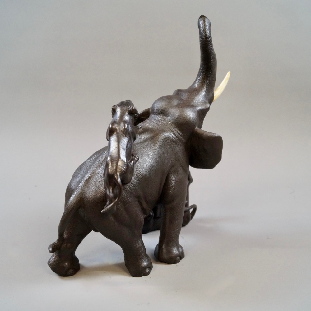 A dark brown patinated bronze okimono sculpture depicting an elephant fighting two tigers, featuring inlaid light tusks. View VII