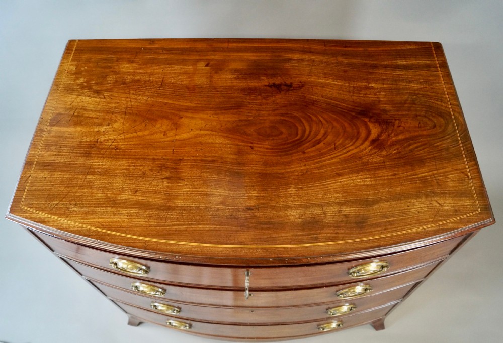 A George III mahogany bow-fronted chest featuring four graduated drawers with oval brass handles and splayed bracket feet. View V