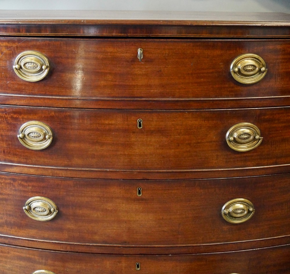 A George III mahogany bow-fronted chest featuring four graduated drawers with oval brass handles and splayed bracket feet. View VI