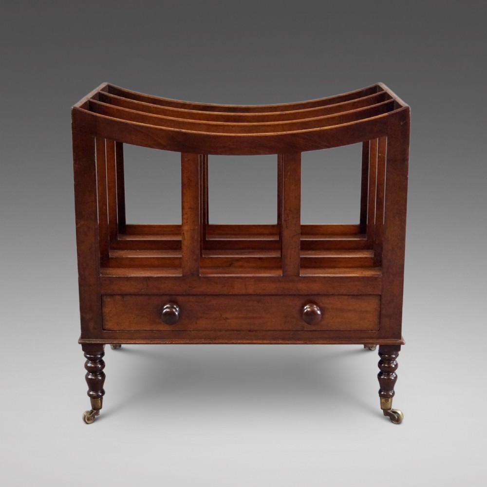 A rich brown Cuban mahogany Canterbury featuring four concave slatted compartments above a single drawer with turned knobs, raised on turned legs with brass castors.