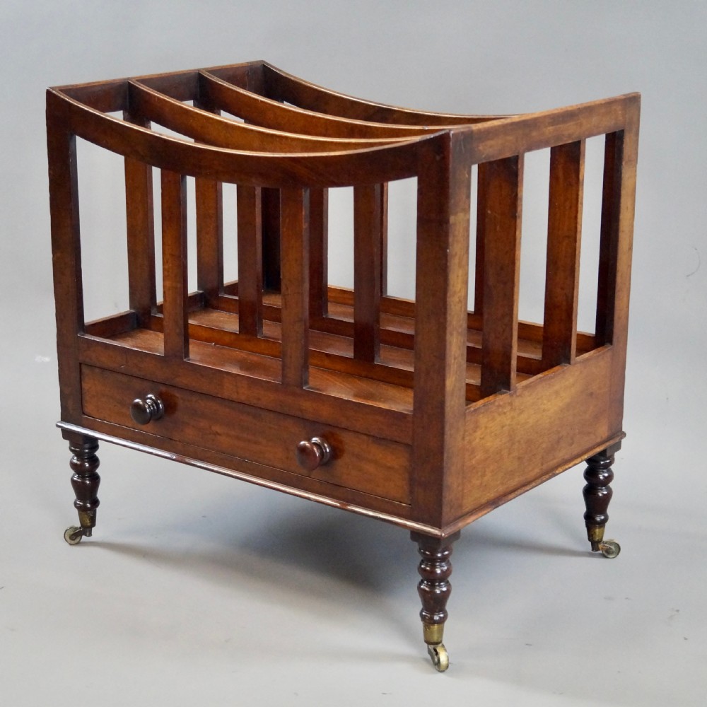 A rich brown Cuban mahogany Canterbury featuring four concave slatted compartments above a single drawer with turned knobs, raised on turned legs with brass castors. View II