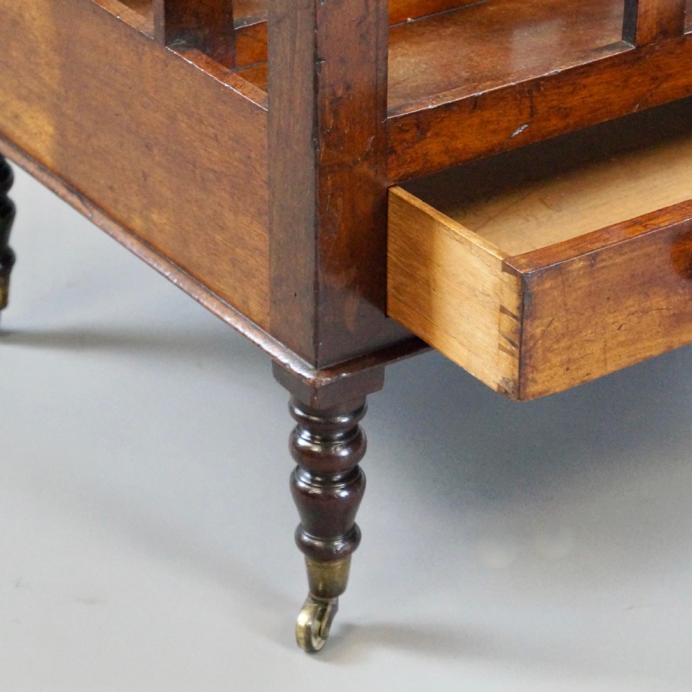 A rich brown Cuban mahogany Canterbury featuring four concave slatted compartments above a single drawer with turned knobs, raised on turned legs with brass castors. View III