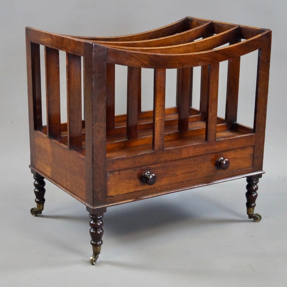 A rich brown Cuban mahogany Canterbury featuring four concave slatted compartments above a single drawer with turned knobs, raised on turned legs with brass castors. View V