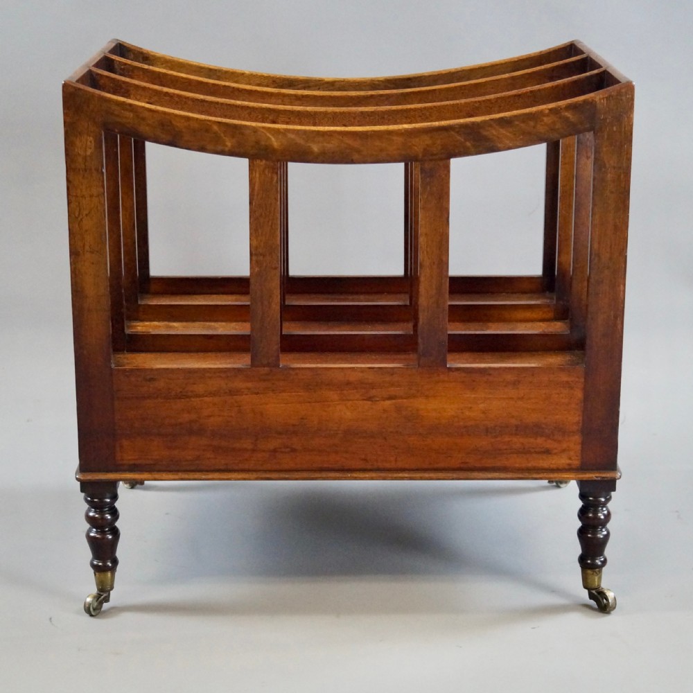A rich brown Cuban mahogany Canterbury featuring four concave slatted compartments above a single drawer with turned knobs, raised on turned legs with brass castors. View VI
