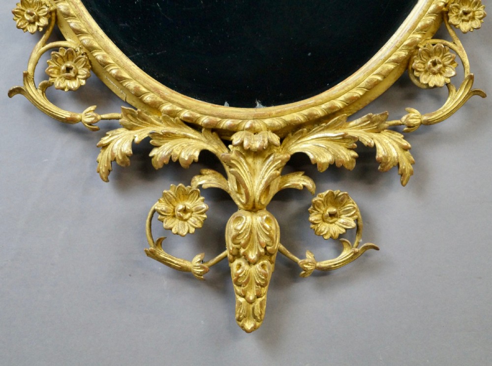A pair of 18th-century oval giltwood wall mirrors featuring carved floral surrounds and fruit-filled urn finials. View VI