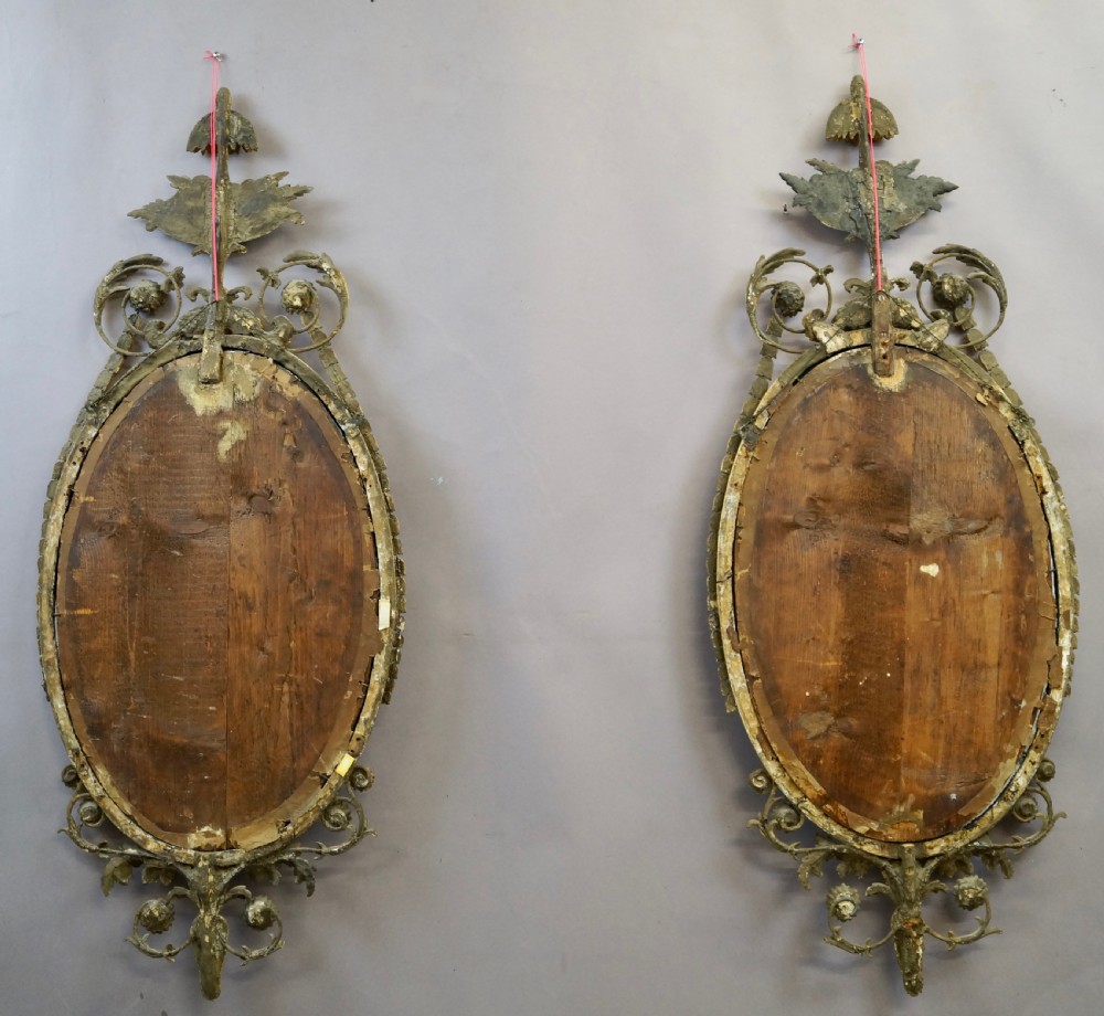 A pair of 18th-century oval giltwood wall mirrors featuring carved floral surrounds and fruit-filled urn finials. View VII