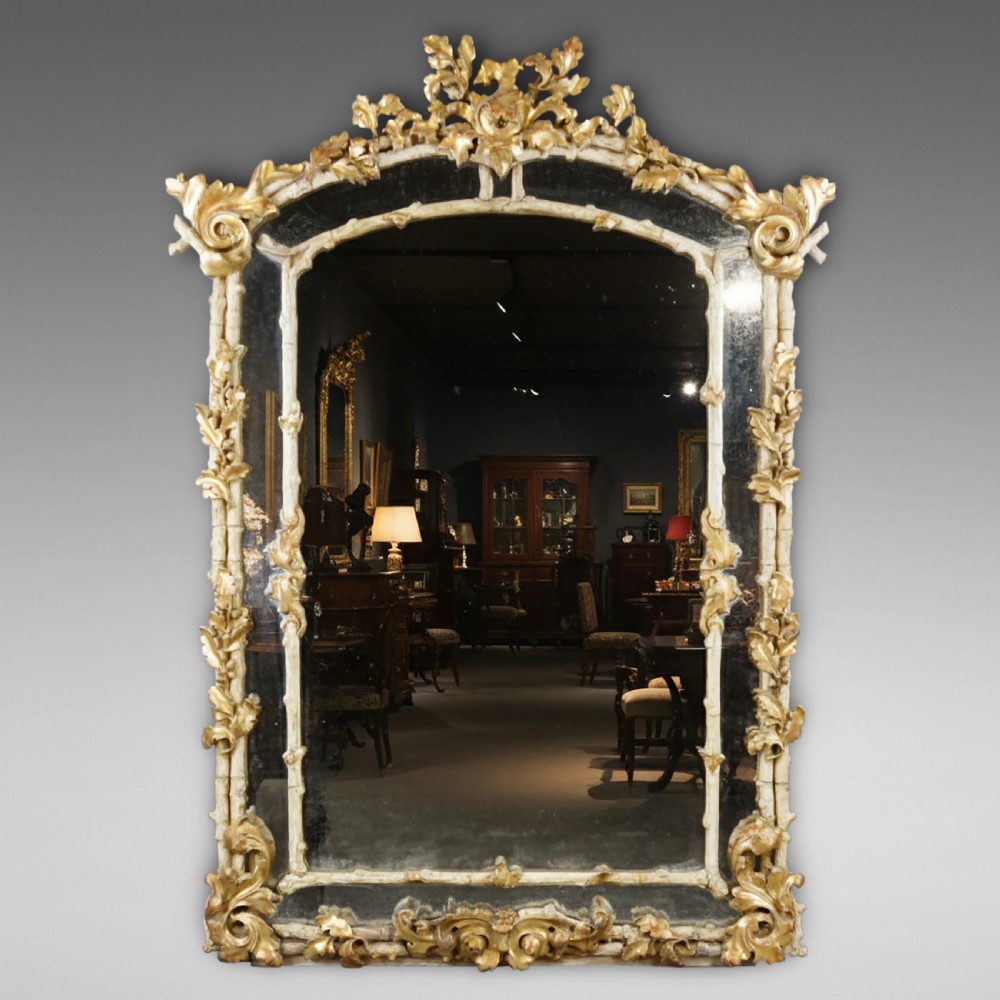 A large 18th-century wall mirror featuring an ornate carved giltwood frame with foliage cresting and a central arched mirror plate.