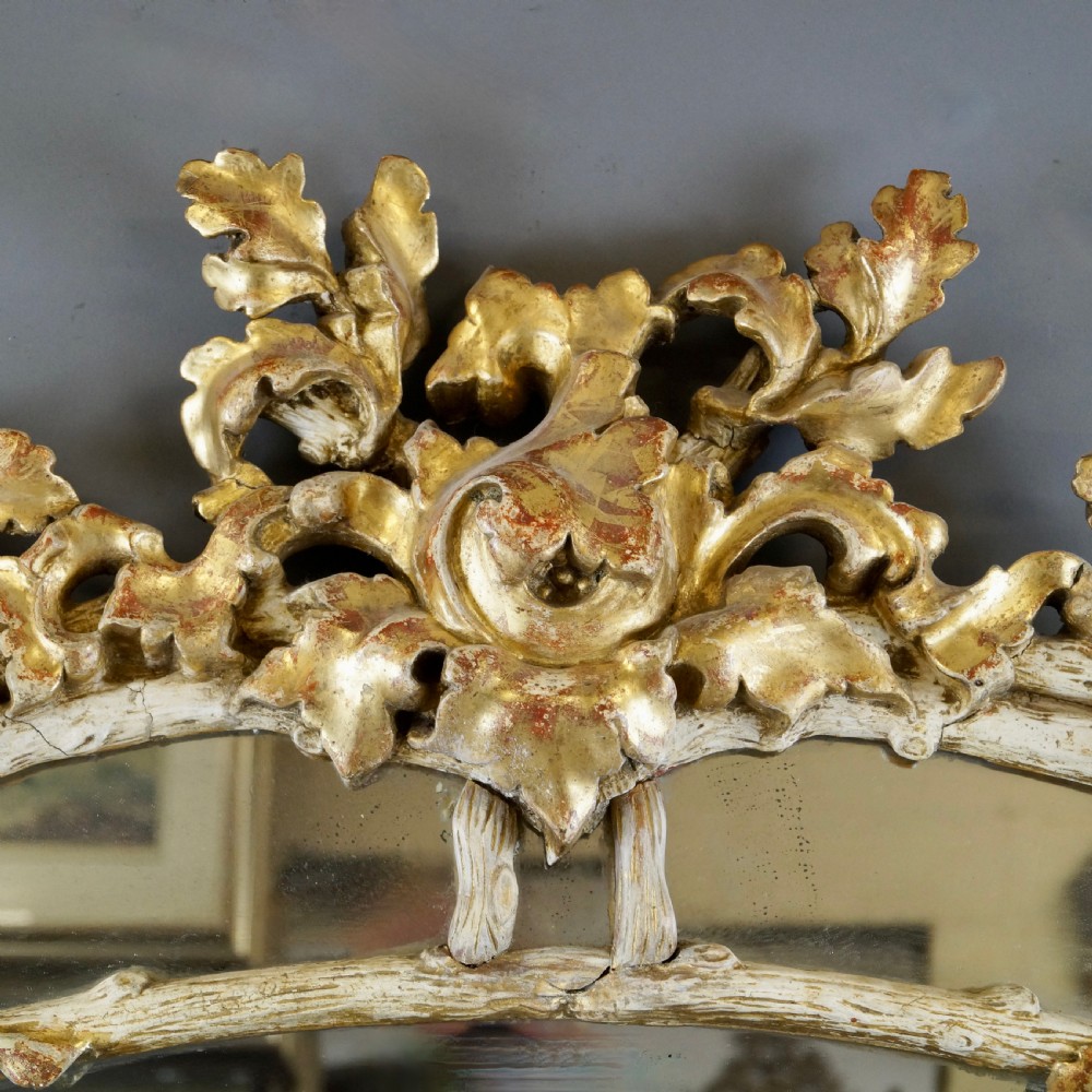 A large 18th-century wall mirror featuring an ornate carved giltwood frame with foliage cresting and a central arched mirror plate. View II