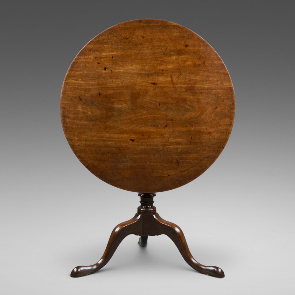 A George III mahogany tripod table featuring a circular tilt top supported by a turned central stem and three cabriole legs.