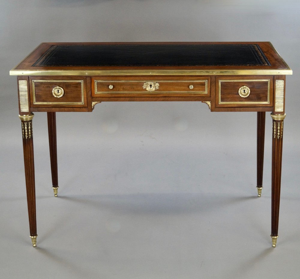 A mahogany writing desk featuring three frieze drawers with brass mounts, a leather-inlaid top, and four tapered fluted legs tipped with brass feet. View II