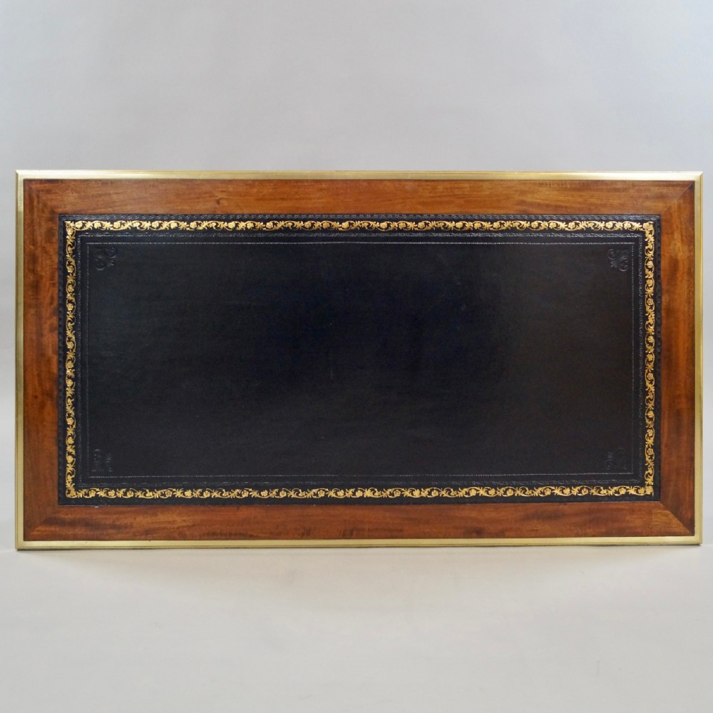 A mahogany writing desk featuring three frieze drawers with brass mounts, a leather-inlaid top, and four tapered fluted legs tipped with brass feet. View VI