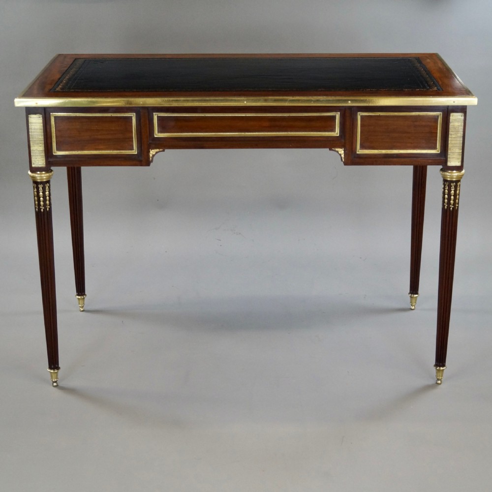 A mahogany writing desk featuring three frieze drawers with brass mounts, a leather-inlaid top, and four tapered fluted legs tipped with brass feet. View VII